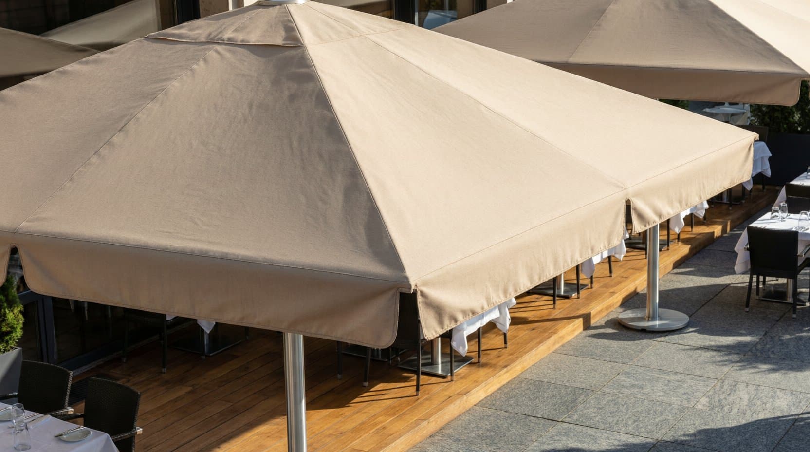 Gastro-Terrasse mit großen quadratischen Sonnenschirmen und gedeckten Tischen